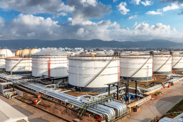 Industrial tanks storing oil and gas at a refinery under a cloudy blue sky